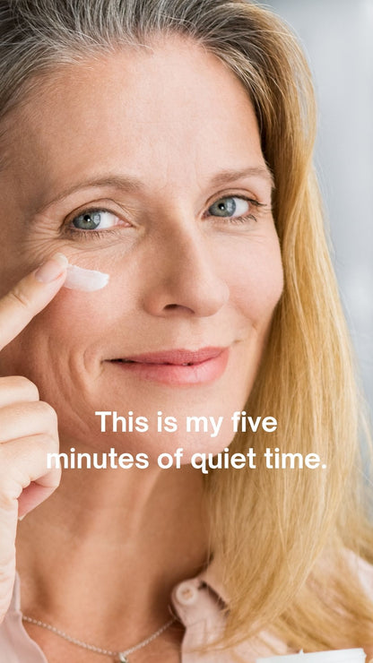 A close-up lifestyle shot of a smiling woman with blonde hair applying a white cream to her cheek. White text overlay reads, 'This is my five minutes of quiet time.
